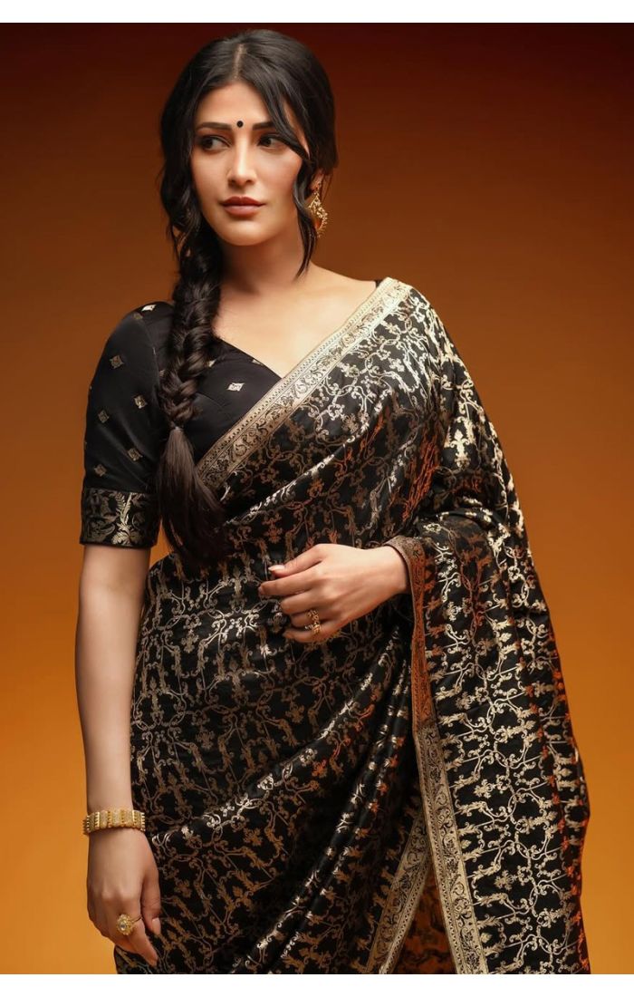 Close-up of woman draped in a black Banarasi silk saree showcasing intricate gold zari designs and detailed blouse work.