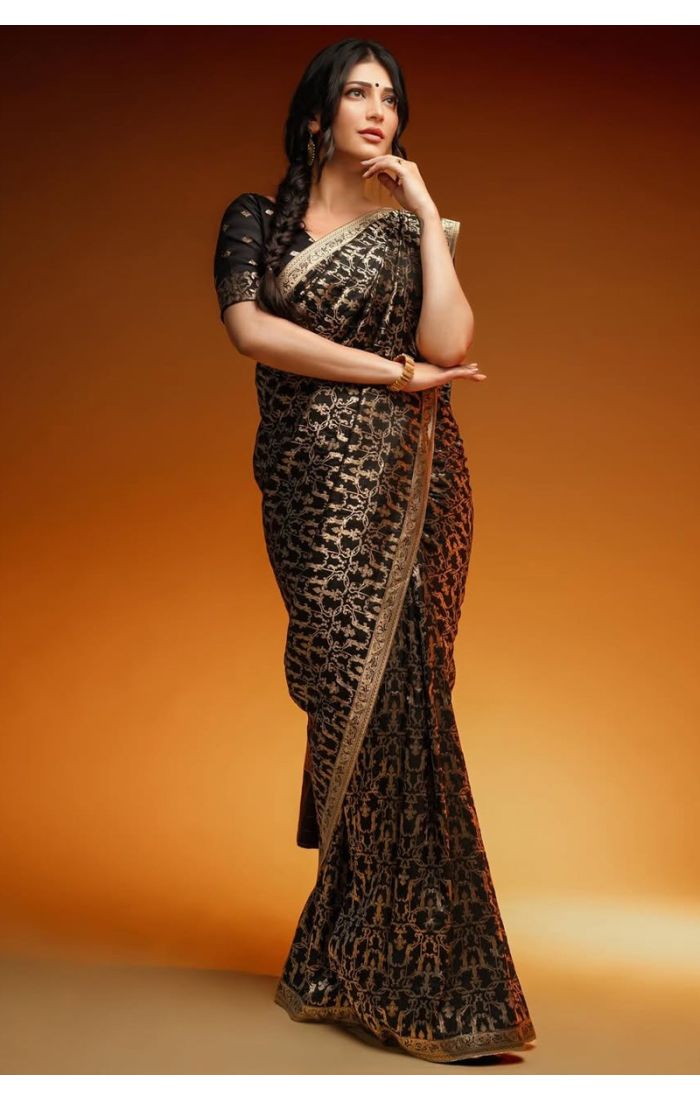Close-up of woman draped in a black Banarasi silk saree showcasing intricate gold zari designs and detailed blouse work.