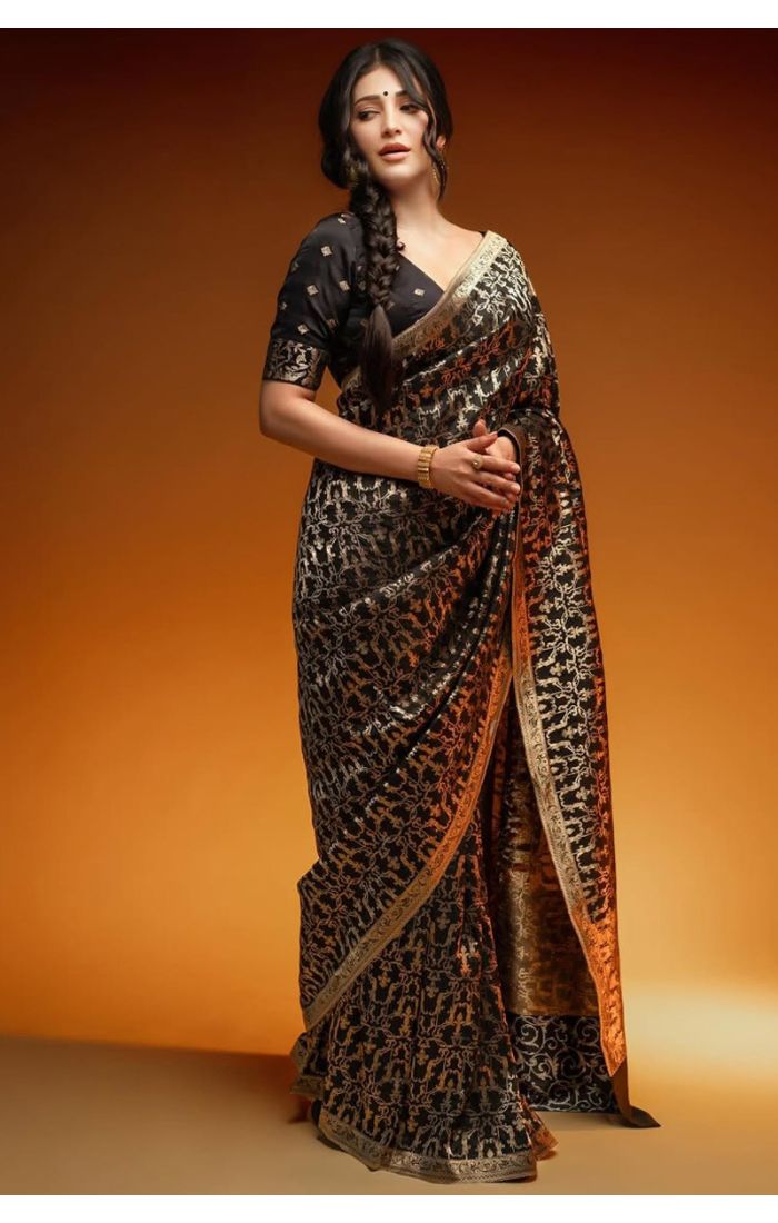 Woman wearing a black Banarasi silk saree with gold zari weaving and traditional gold border, styled with a black blouse, posing elegantly.