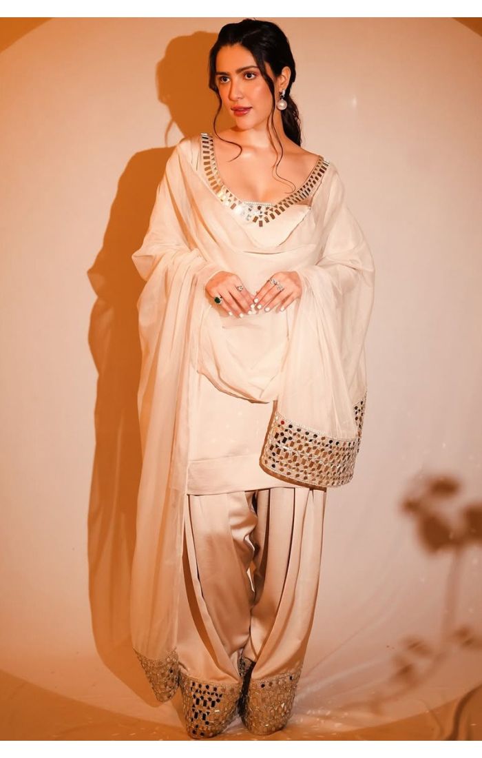 Woman wearing an ivory georgette sharara suit with mirror work, styled with pearl earrings and a matching mirror work clutch.