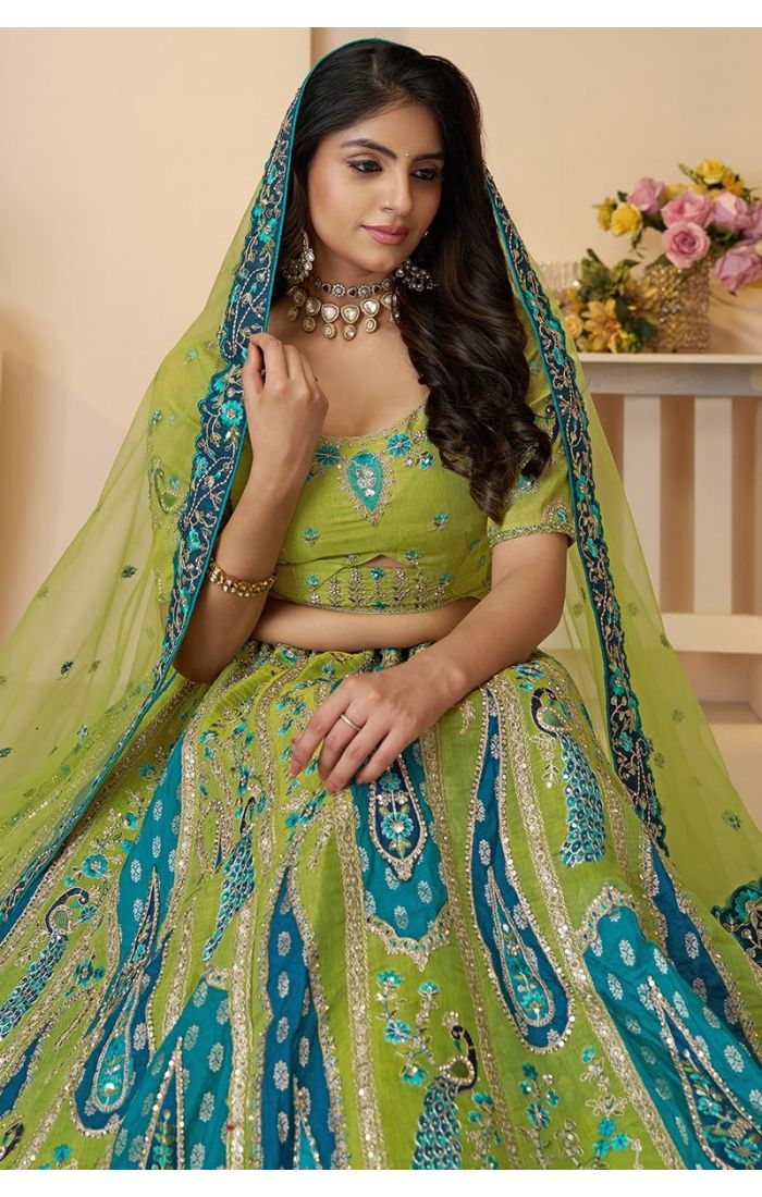 Front pose of the model wearing a green and blue embroidered net lehenga with paisley and peacock motifs.