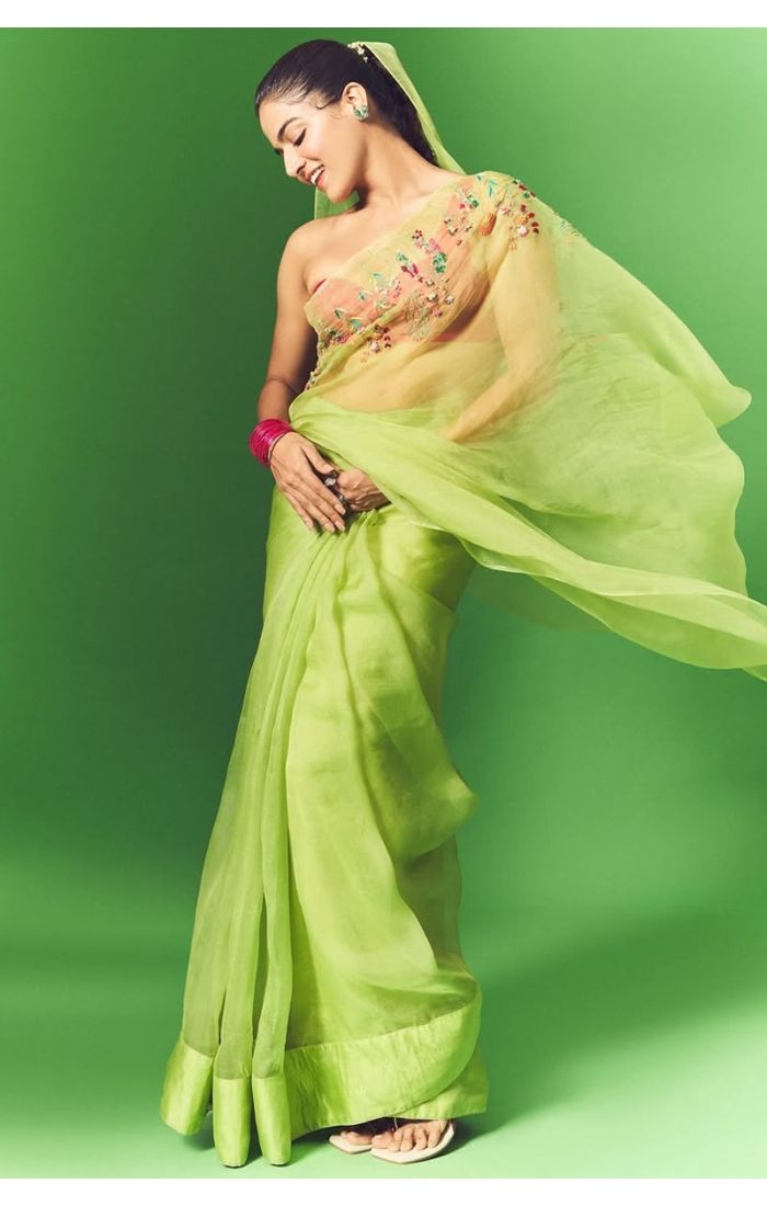 Side close-up of model in light green organza saree with multicolor floral embroidery and statement rings.